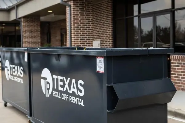 Dark front-load commercial dumpster next to a brick storefront entrance