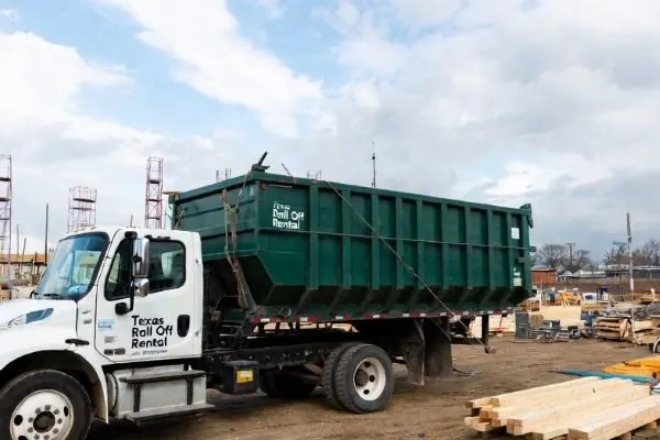 Roll-off truck carrying a green open-top container across a construction lot